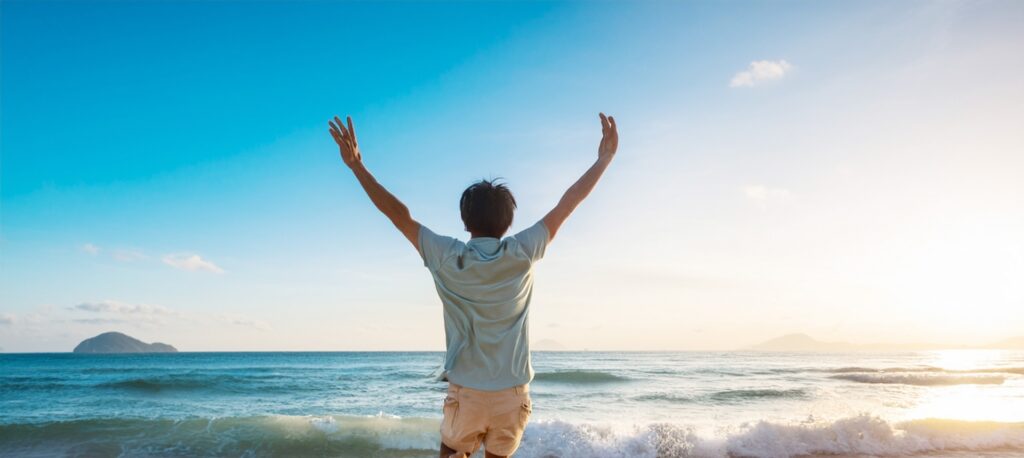 海辺で両手をあげる男性
